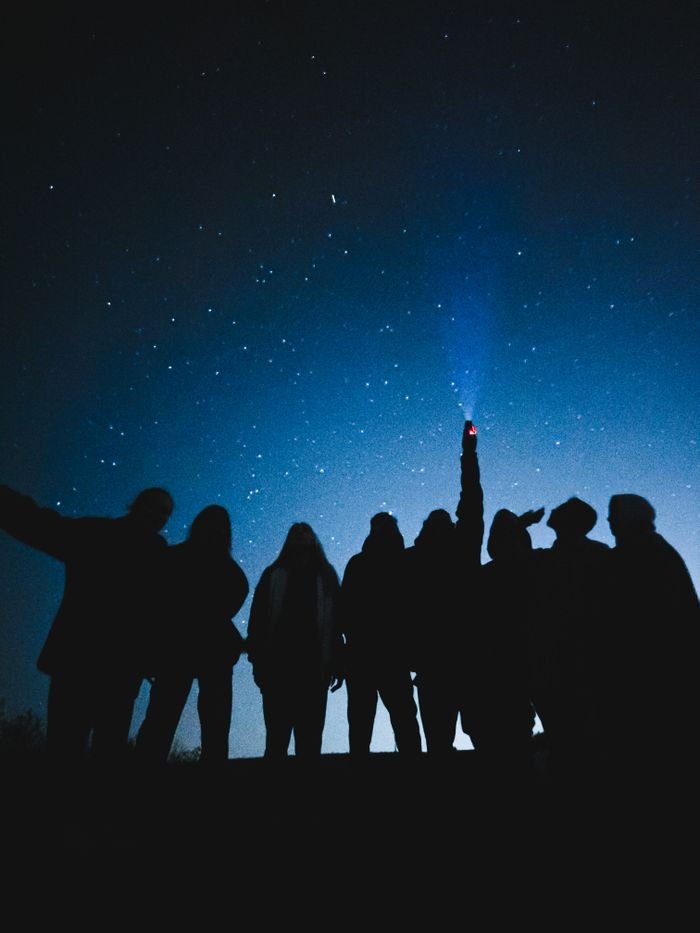 services-img A group of silhouetted people stargazing at a clear night sky, one pointing a flashlight upwards.