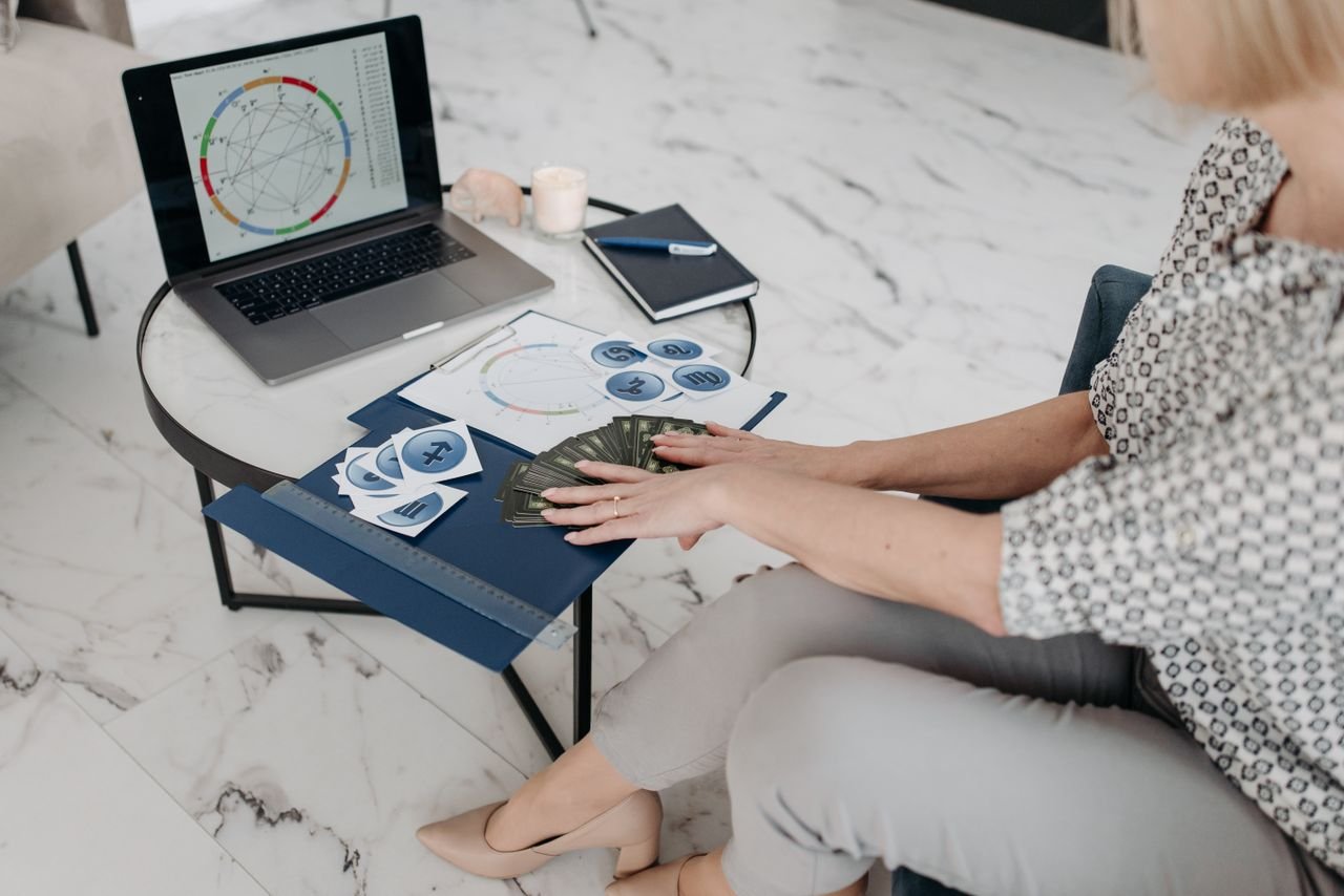 services-04 Astrology scene with a woman using a laptop and tarot cards in a modern living room.